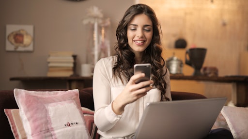Woman Sitting On Sofa While Looking At Phone With Laptop On 920382