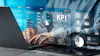 Professional analyzing KPI metrics on laptop with holographic business dashboard displaying charts, graphs, and analytics data