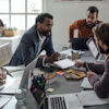 Diverse team of professionals collaborating during a business meeting at a conference table with laptops and documents.