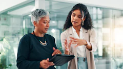 Two professional women discussing business strategy in a modern glass office environment