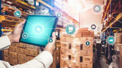 Worker holding tablet with digital logistics icons in warehouse with stacked boxes