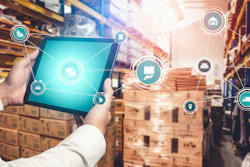 Worker holding tablet with digital logistics icons in warehouse with stacked boxes