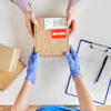 Worker in blue gloves processing a return shipment with cardboard boxes and clipboard on white surface