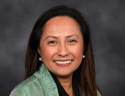Professional headshot of a smiling woman with long dark hair wearing a green blazer and pearl earrings