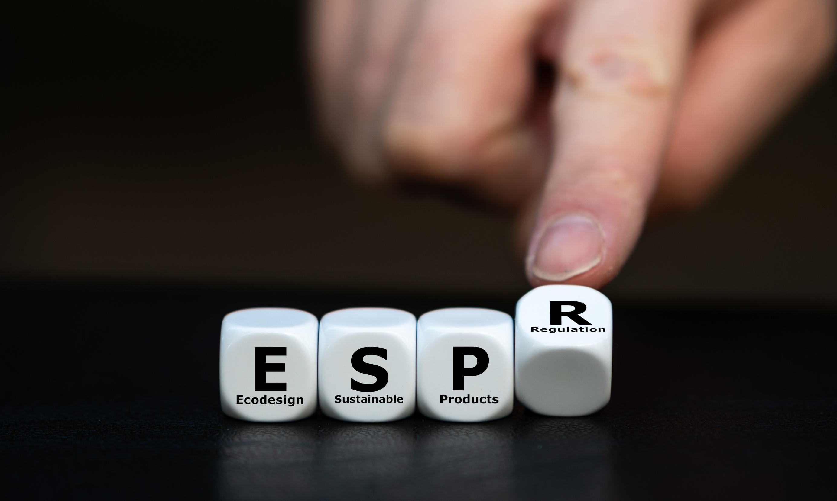 Hand pointing to white cubes spelling ESP (Ecodesign Sustainable Products) with R Regulation cube on dark surface