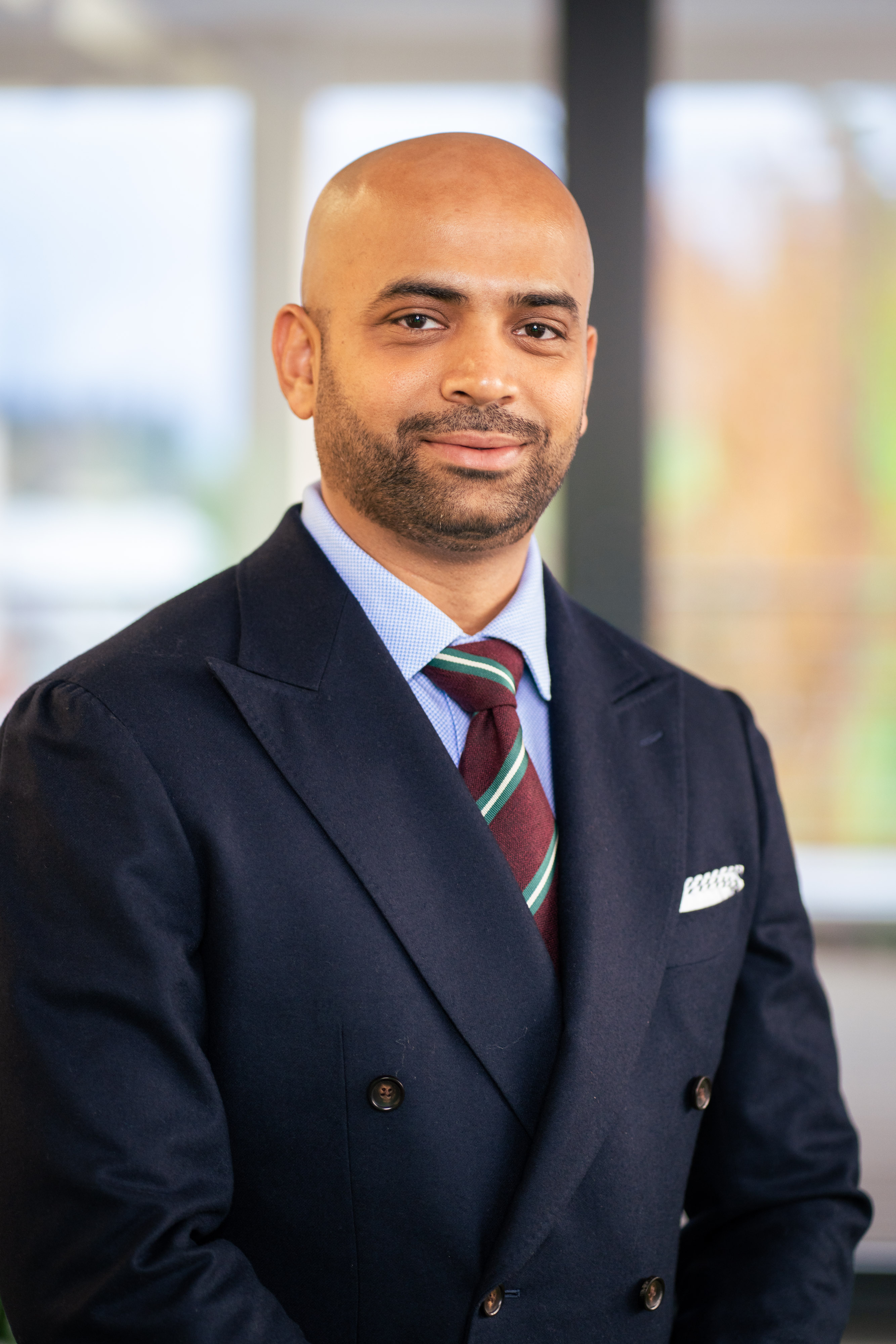 Professional man in navy blazer and burgundy striped tie smiling at camera in modern office setting Headshot