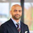 Professional man in navy blazer and burgundy striped tie smiling at camera in modern office setting Headshot