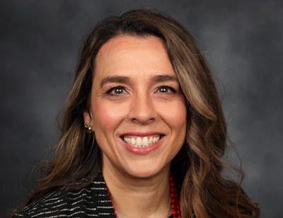 Professional headshot of a smiling woman with long brown hair wearing a red and black striped jacket