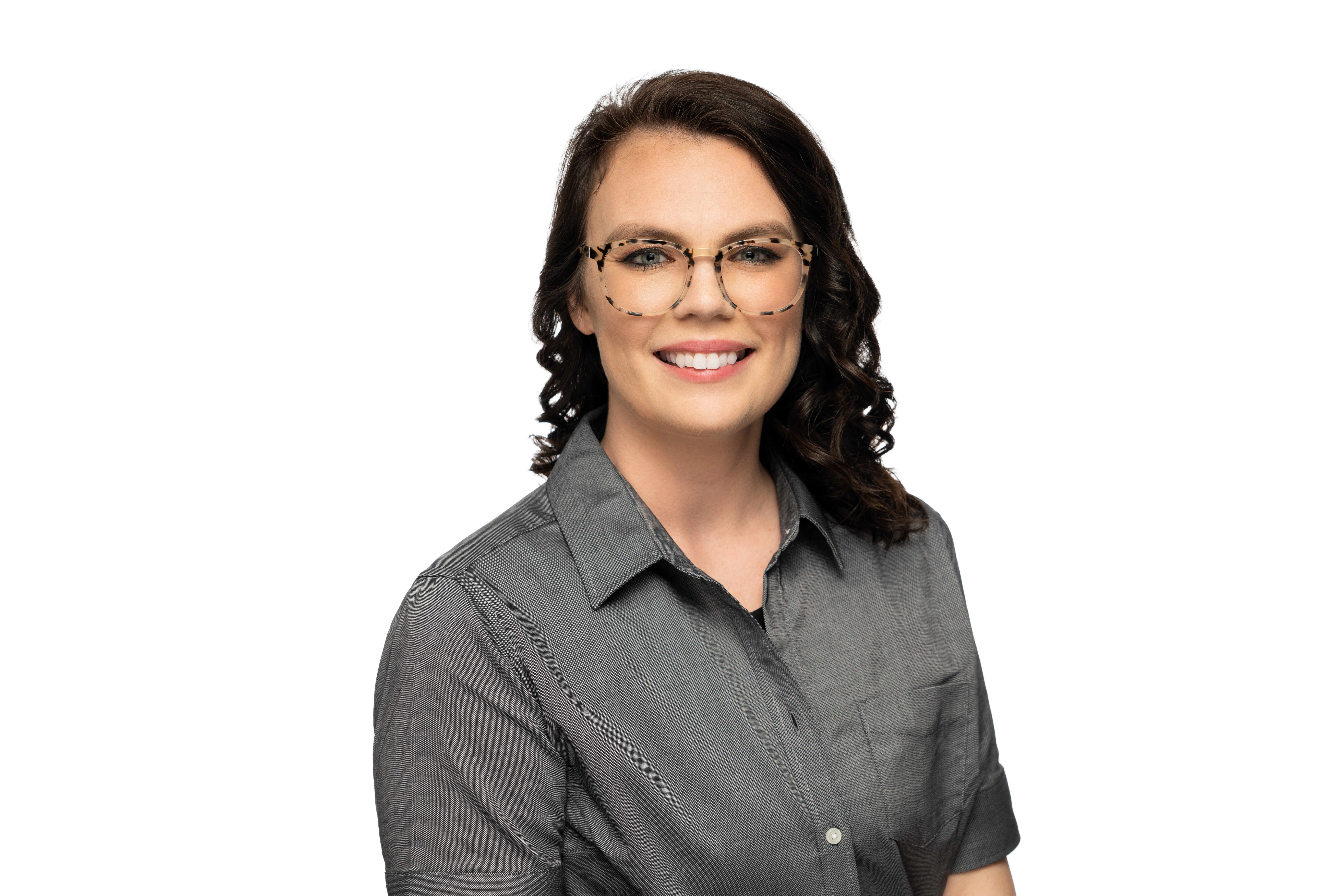 Professional headshot of a woman wearing glasses and a gray button-up shirt, smiling at camera