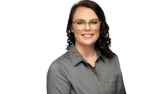 Professional headshot of a woman wearing glasses and a gray button-up shirt, smiling at camera