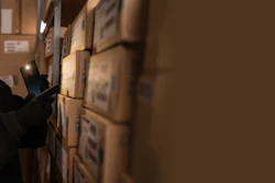 Person in dark winter gear examining cardboard boxes in warehouse storage facility