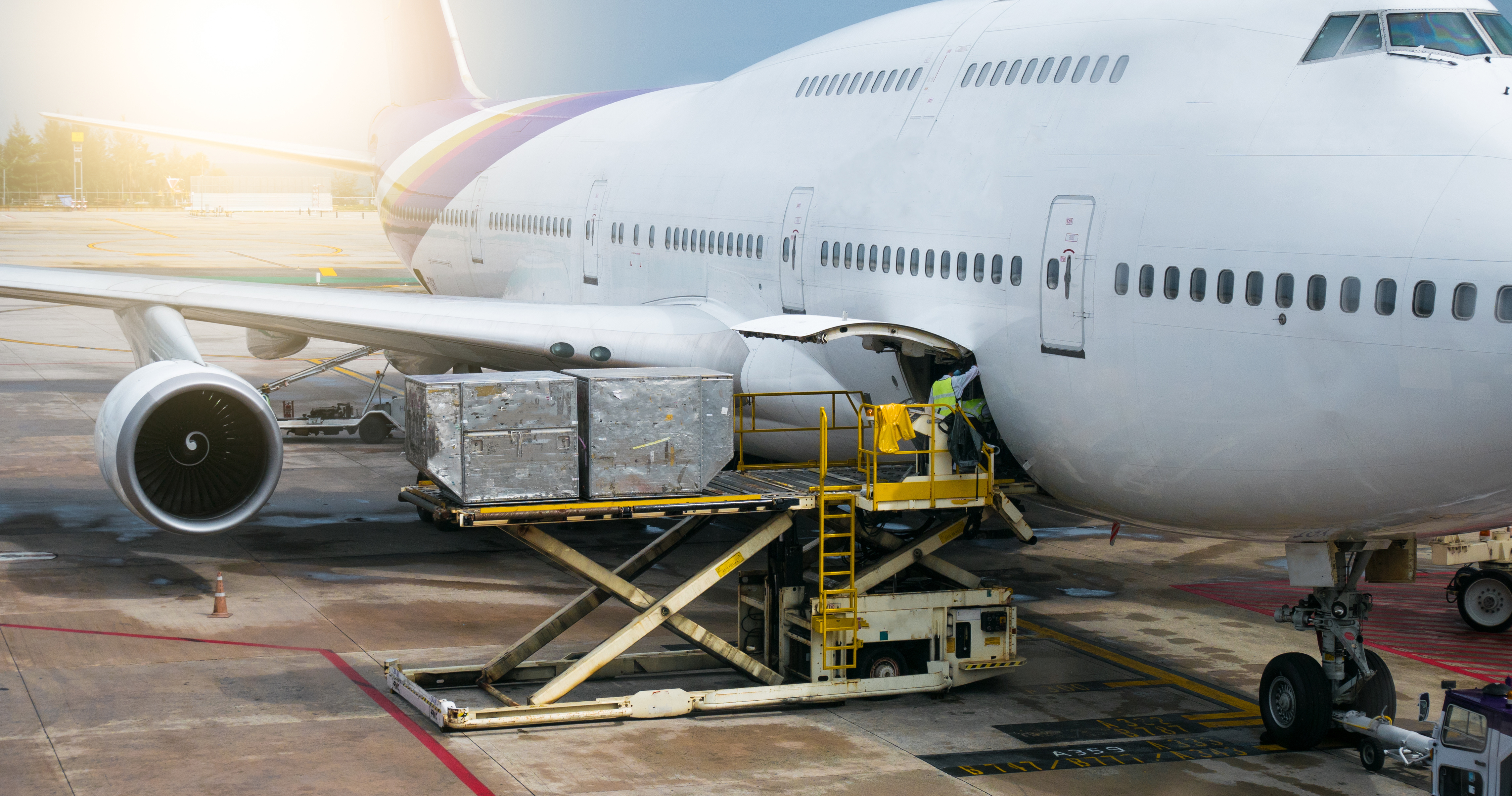 Cargo loader transferring freight containers to wide-body aircraft at airport during daytime operations