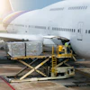 Cargo loader transferring freight containers to wide-body aircraft at airport during daytime operations