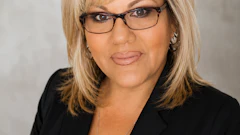 Professional headshot of a woman wearing glasses and black blazer against neutral background
