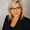Professional headshot of a woman wearing glasses and black blazer against neutral background