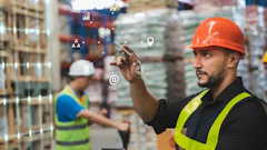 Warehouse worker in orange hard hat and safety vest using tablet with digital business analytics icons overlay