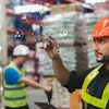 Warehouse worker in orange hard hat and safety vest using tablet with digital business analytics icons overlay