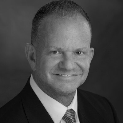 Professional headshot of a man in business suit and tie against gray background Headshot