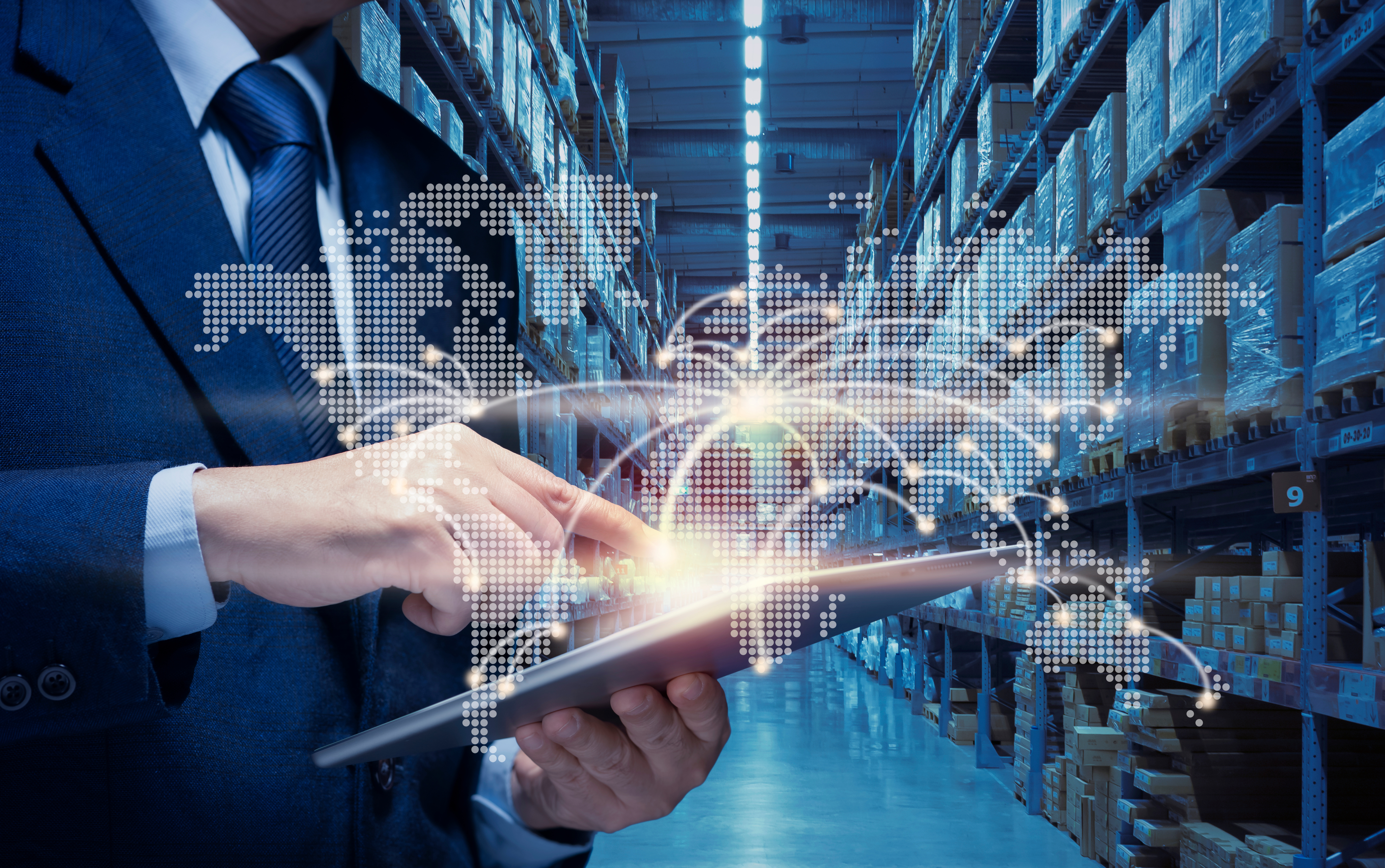 Businessman holding tablet in warehouse with holographic world map and global network visualization overlay