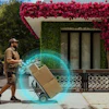 Delivery worker pushing hand truck with package outside modern storefront with red flowering vines and digital AR visualization effect