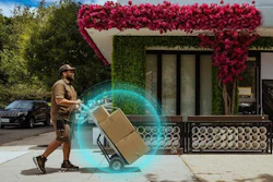Delivery worker pushing hand truck with package outside modern storefront with red flowering vines and digital AR visualization effect