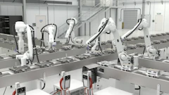 Industrial robotic assembly line with white mechanical arms processing components on a production conveyor in a modern factory facility.