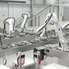 Industrial robotic assembly line with white mechanical arms processing components on a production conveyor in a modern factory facility.
