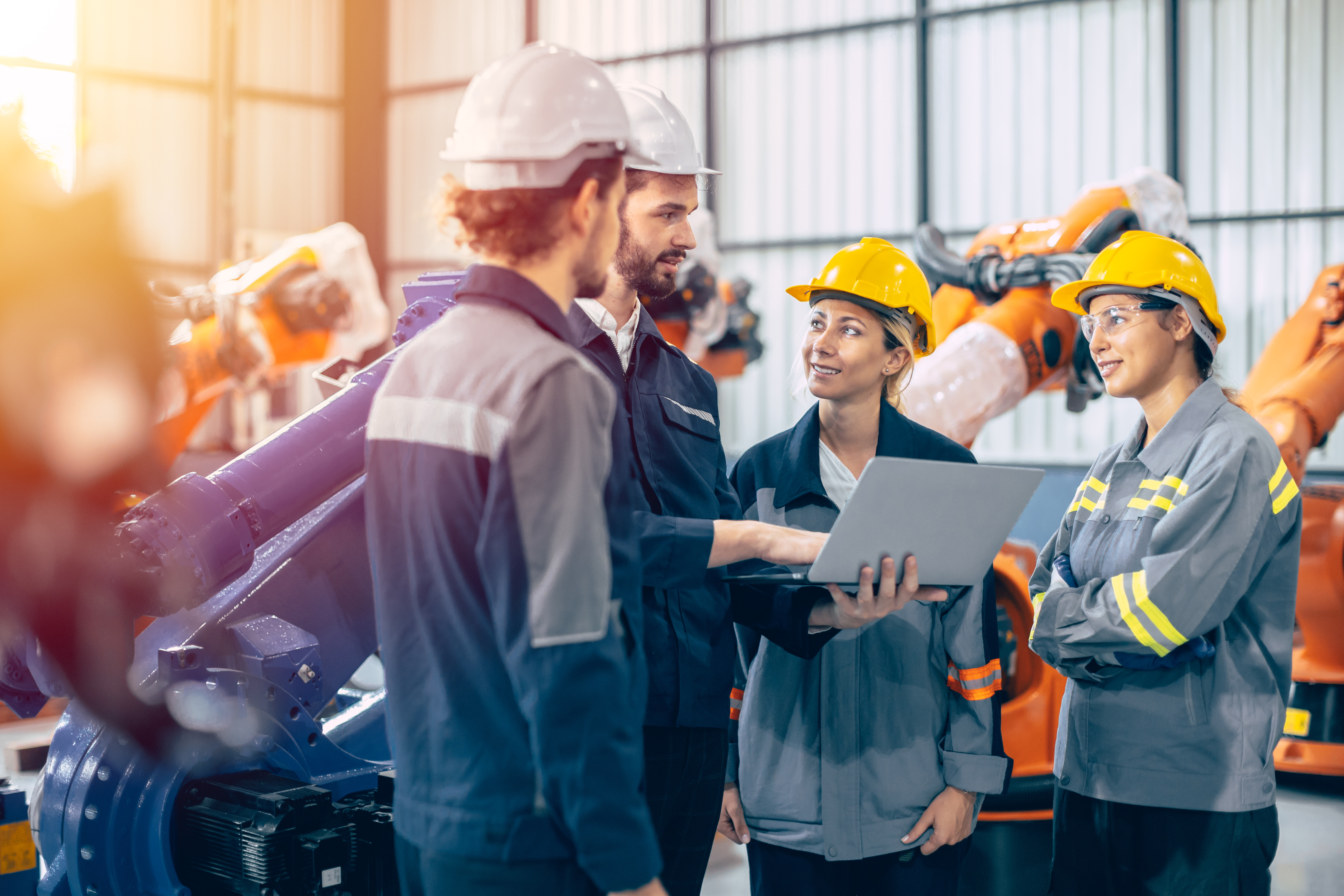 Construction team reviewing plans on laptop in industrial warehouse with safety equipment