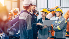 Construction team reviewing plans on laptop in industrial warehouse with safety equipment