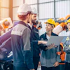 Construction team reviewing plans on laptop in industrial warehouse with safety equipment
