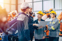Construction team reviewing plans on laptop in industrial warehouse with safety equipment