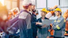 Construction team reviewing plans on laptop in industrial warehouse with safety equipment