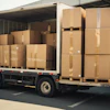 White delivery truck loaded with stacked cardboard boxes on wooden pallets in warehouse setting