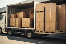 White delivery truck loaded with stacked cardboard boxes on wooden pallets in warehouse setting