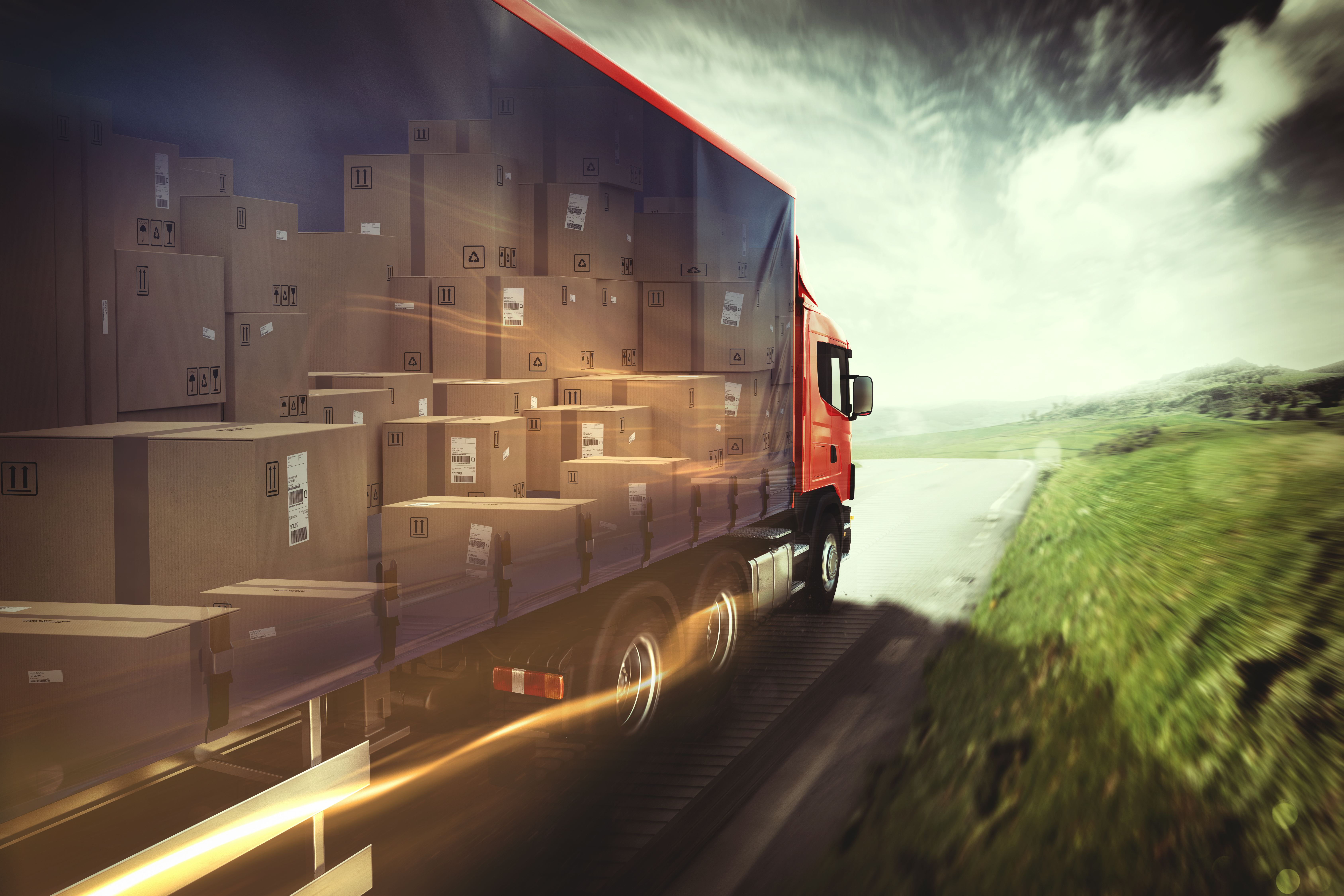 Red delivery truck loaded with cardboard boxes driving on highway with green landscape and dramatic sky