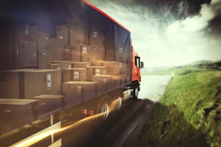 Red delivery truck loaded with cardboard boxes driving on highway with green landscape and dramatic sky