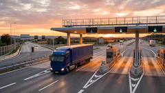 Trucks passing through highway toll booths at sunset with overpass and multiple lanes