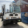 White industrial forklift with blue cabin parked in warehouse with shipping containers