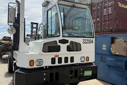 White industrial forklift with blue cabin parked in warehouse with shipping containers