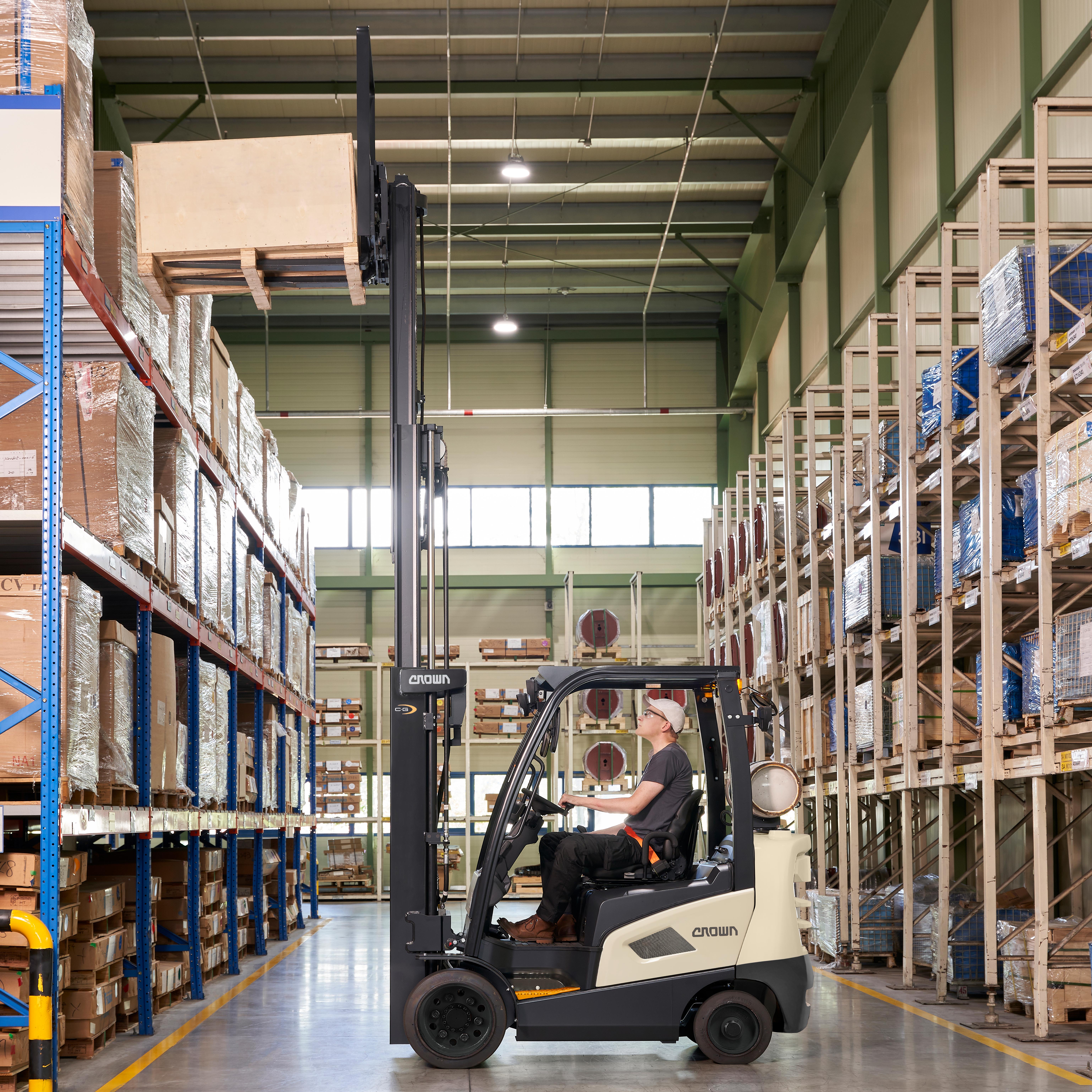 Forklift operator moving cargo in a large warehouse with blue and metal shelving units.