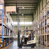 Forklift operator moving cargo in a large warehouse with blue and metal shelving units.
