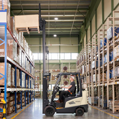 Forklift operator moving cargo in a large warehouse with blue and metal shelving units.