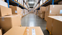 Industrial warehouse aisle lined with stacked cardboard boxes on blue and yellow metal shelving units