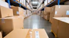Industrial warehouse aisle lined with stacked cardboard boxes on blue and yellow metal shelving units