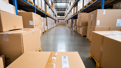 Industrial warehouse aisle lined with stacked cardboard boxes on blue and yellow metal shelving units