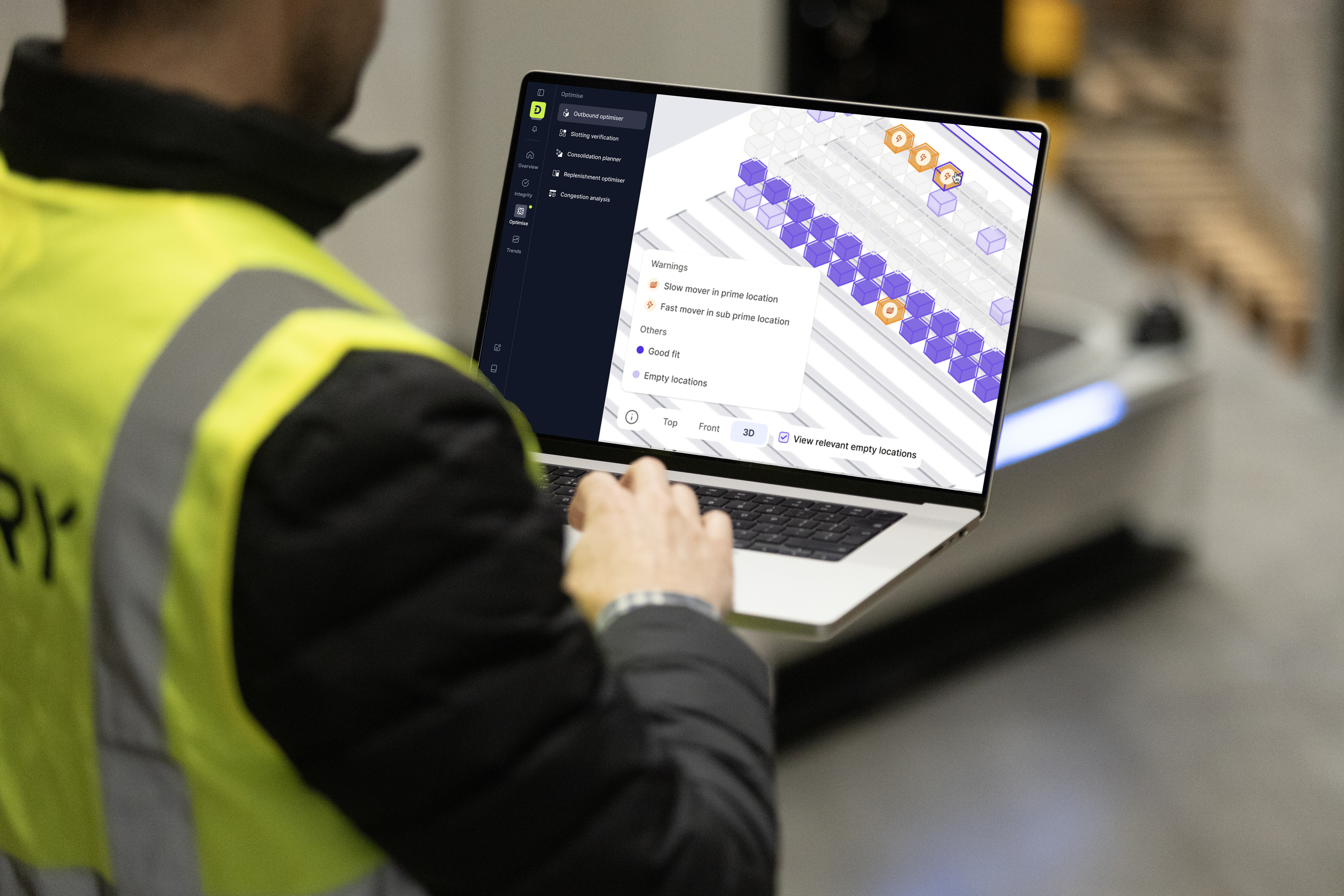 Worker in high-visibility vest using laptop displaying purple and orange data visualization interface in warehouse setting