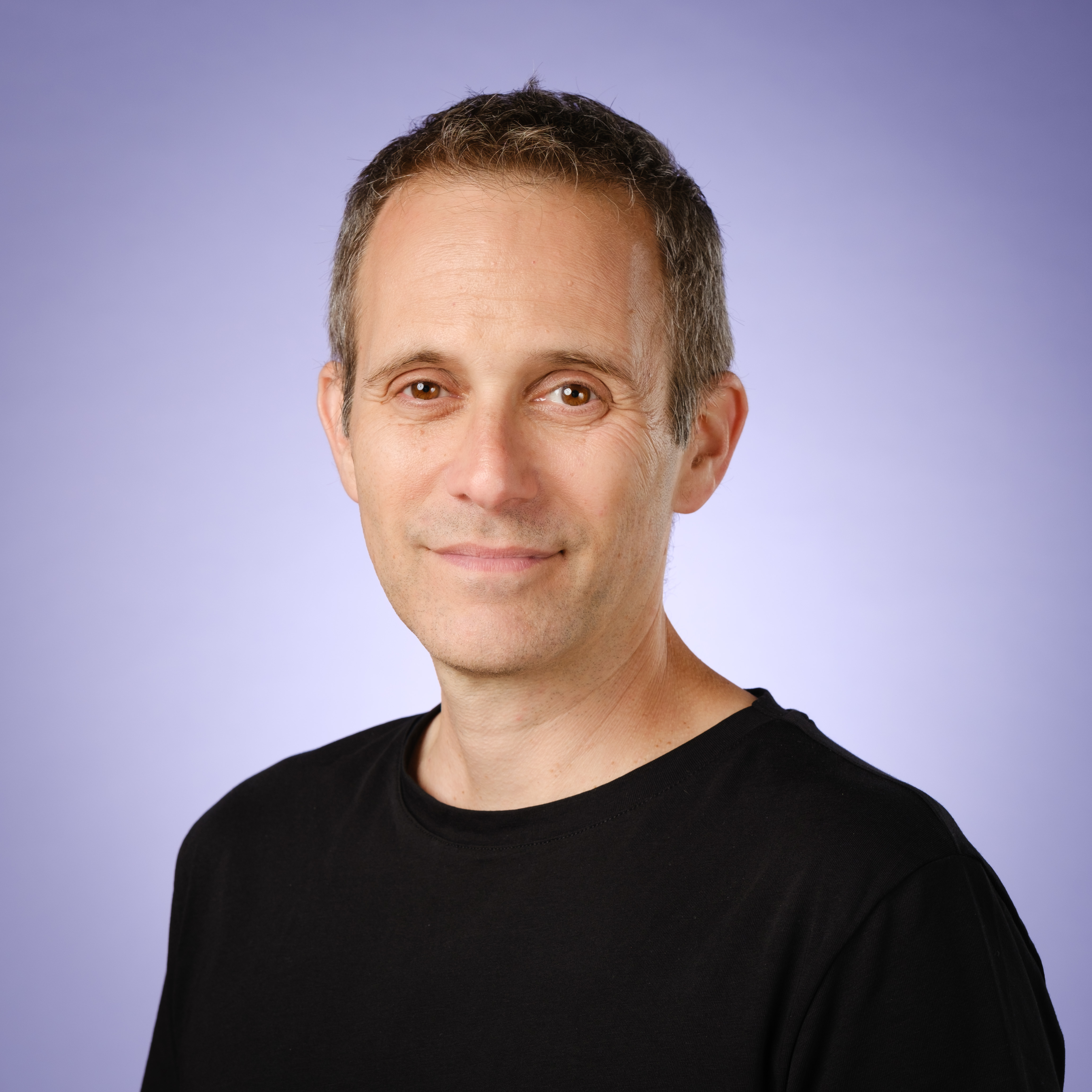 Professional headshot of a middle-aged man wearing a black t-shirt against a purple gradient background