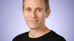 Professional headshot of a middle-aged man wearing a black t-shirt against a purple gradient background