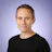 Professional headshot of a middle-aged man wearing a black t-shirt against a purple gradient background Headshot