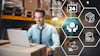 Man working on laptop in warehouse with supply chain logistics icons representing delivery, tracking, and quality management